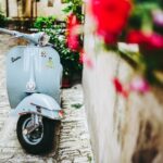 selective focus photo of blue motor scooter beside concrete wall