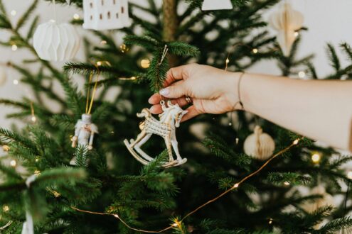 A person decorating a Christmas tree with ornaments, creating a festive holiday atmosphere.